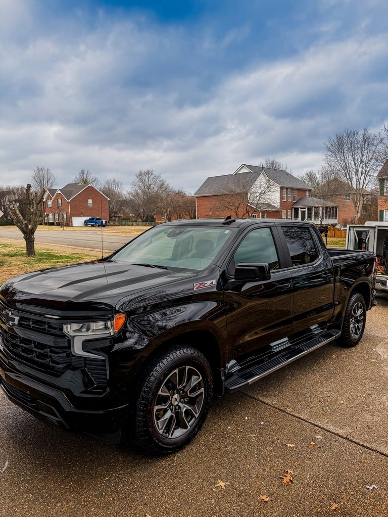 Black Chevrolet pickup truck parked in driveway with residential homes and bare trees in background
