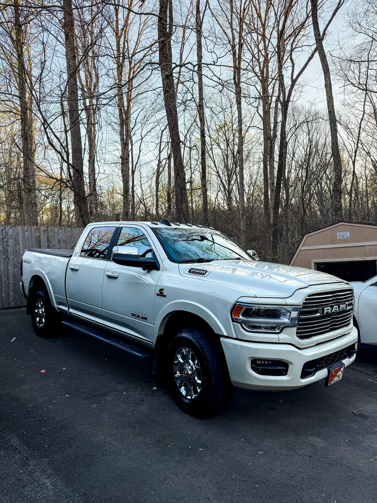 White Ram pickup truck parked in a lot with bare trees in the background and a garage visible to the right