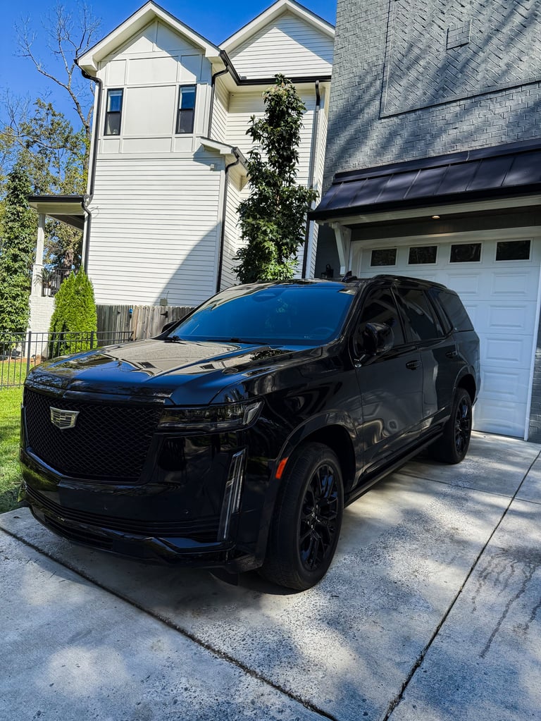 Black Cadillac SUV parked in driveway in front of white two-story house with garage