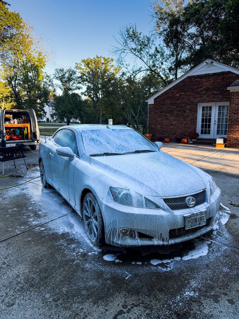 White Lexus sedan covered in soap suds during car wash in residential driveway